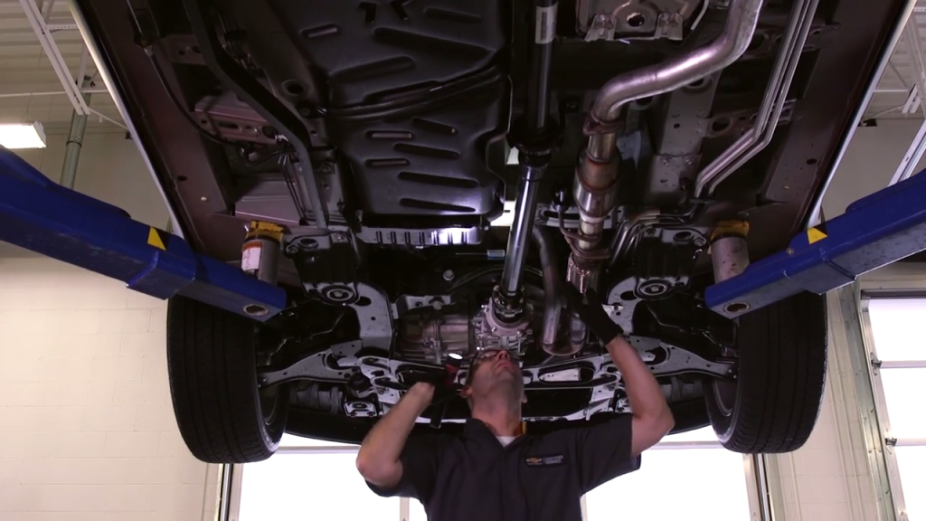 Mechanic inspecting the underside of a car on a lift in a service bay.